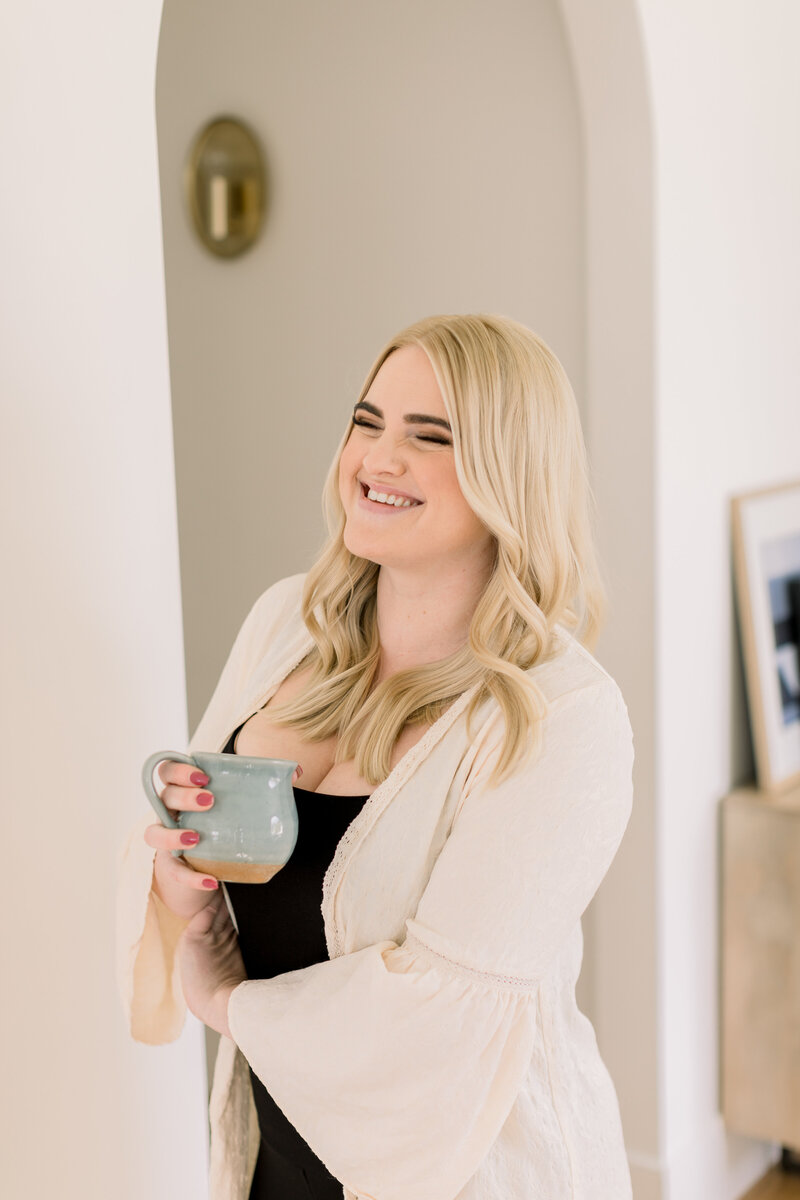 Therapist Megan Zuzevich stands with her hand on the wall in a hallway, smiling to the camera. She helps people in the Los Angeles County area heal from trauma, vicarious traumatization, anxiety and more with EMDR therapy in California.