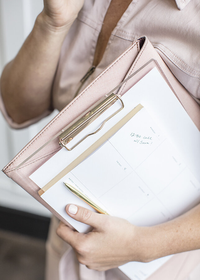 Woman holding a pink clipboard and a gold pen