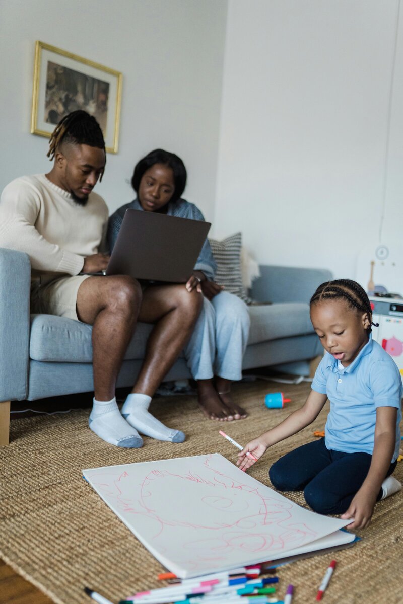 man and woman on the computer while watching their child