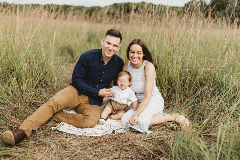 Smiling father holding two young children in fall outfits during an outdoor family photo session  in Maple Grove, Minnesota