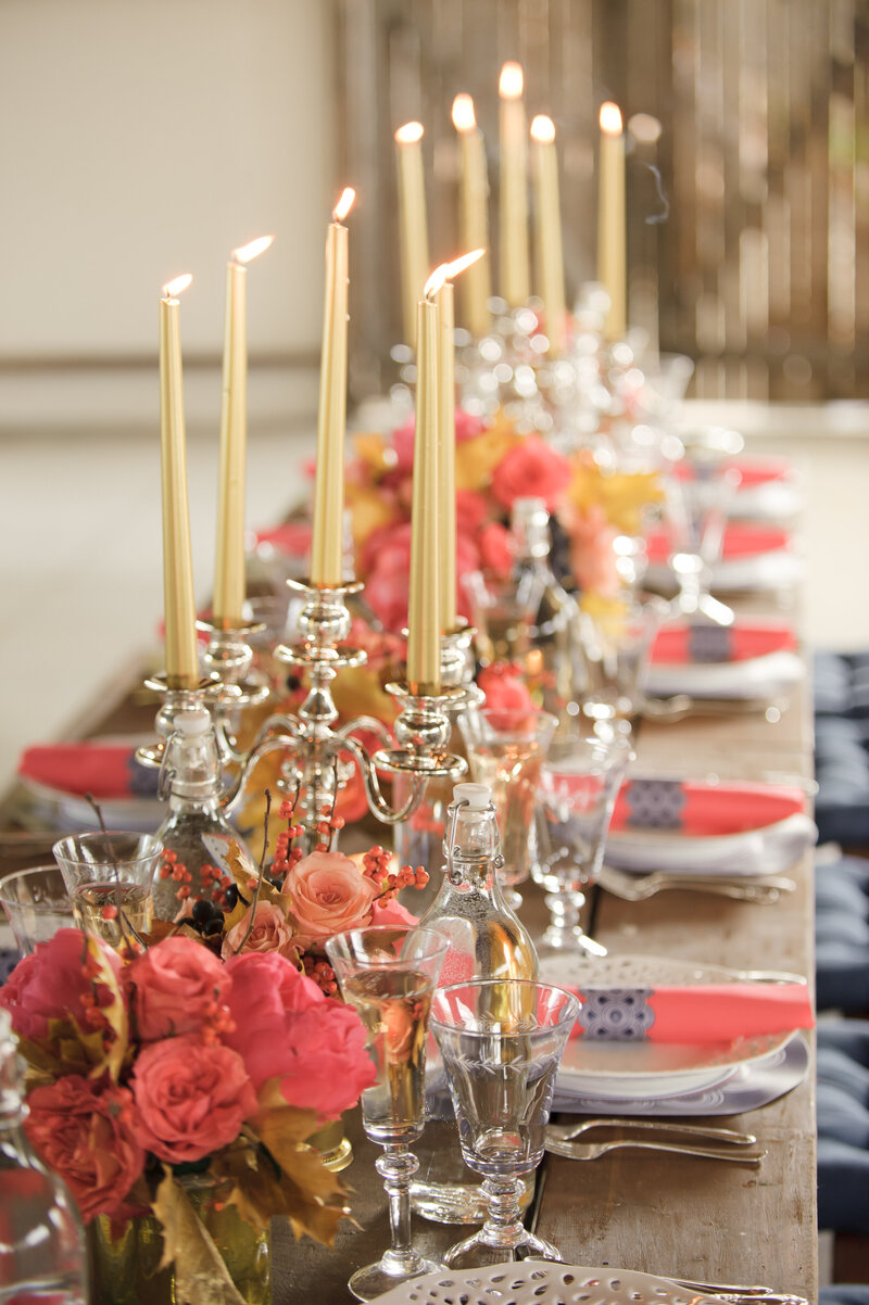 Elegant dining table adorned with tall candles, vibrant floral arrangements, and finely set dinnerware for a festive celebration.