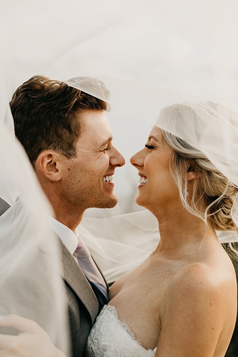Eloping couple smiling at each other while under the veil