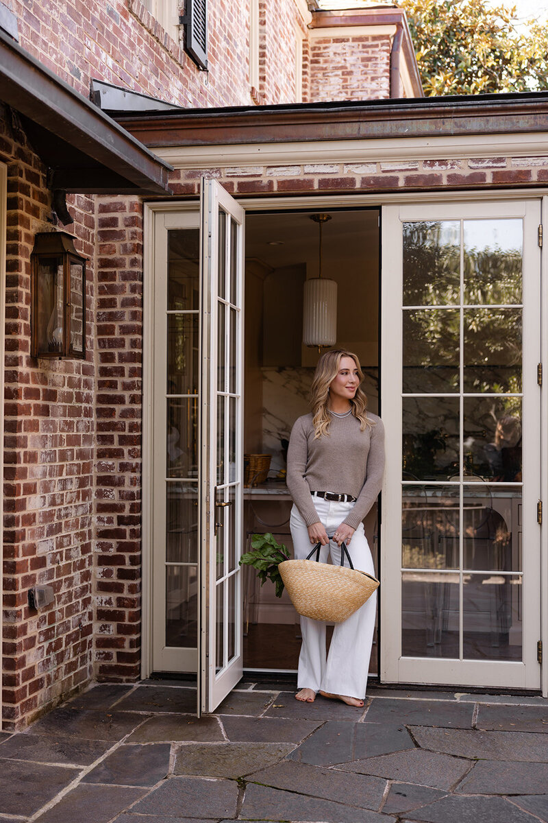 unctional dietician and nutritionist Tracy Greenstein holding a basket of nourishing fruits, vegetables, and herbs while standing in a French door entryway