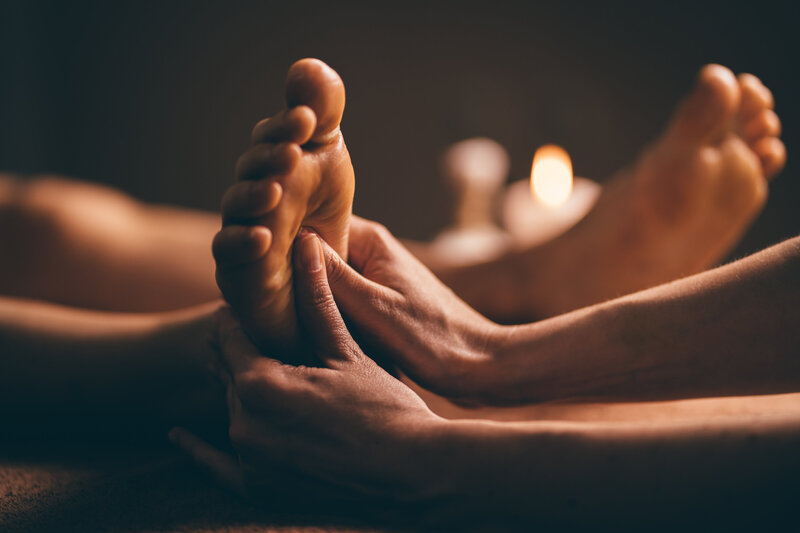 Therapist performing foot reflexology massage in a softly lit, calming spa environment.