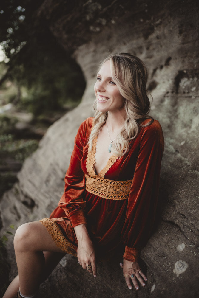 Soft portrait of Caroline leaning against a cliff, embodying trust, inner strength, and connection to earth energy.