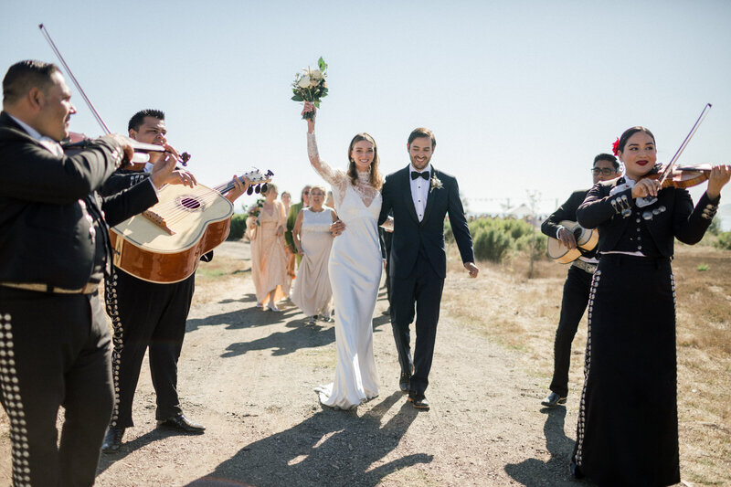 couple being serenaded by Mariachi band as they smile and walk from wedding ceremony