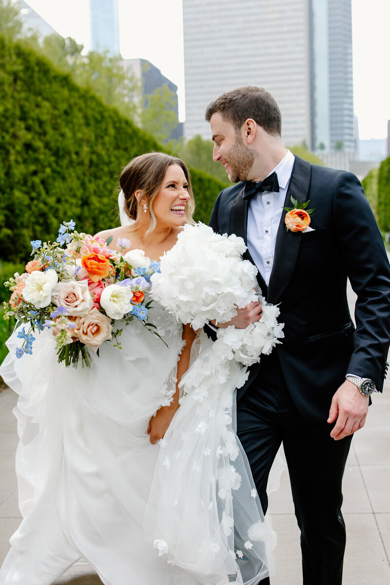 Bride and groom smile at each other while walking down Chicago park path