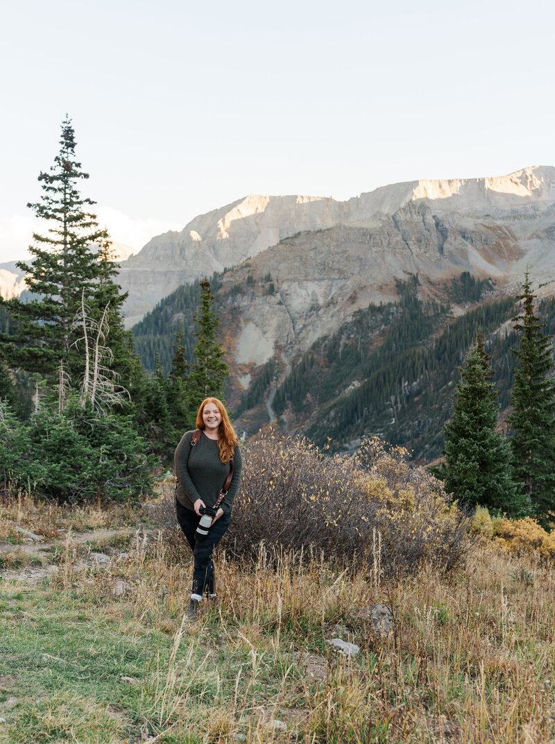 Samantha Immer stands in a field of wildflowers holding her camera in Colorado
