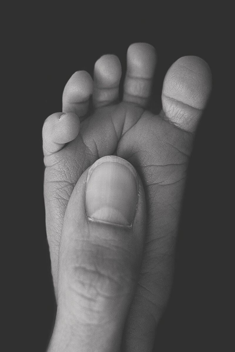 newborn baby foot with moms thumb
