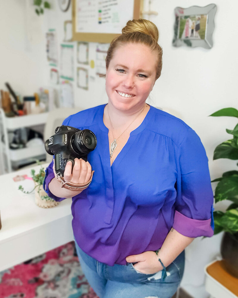 Photographer stands in home office holding camera