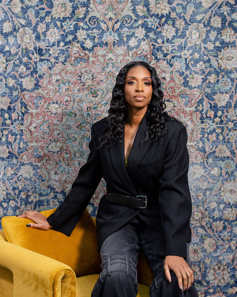 Shaniece Jones sat on the arm of a yellow sofa looking serious.