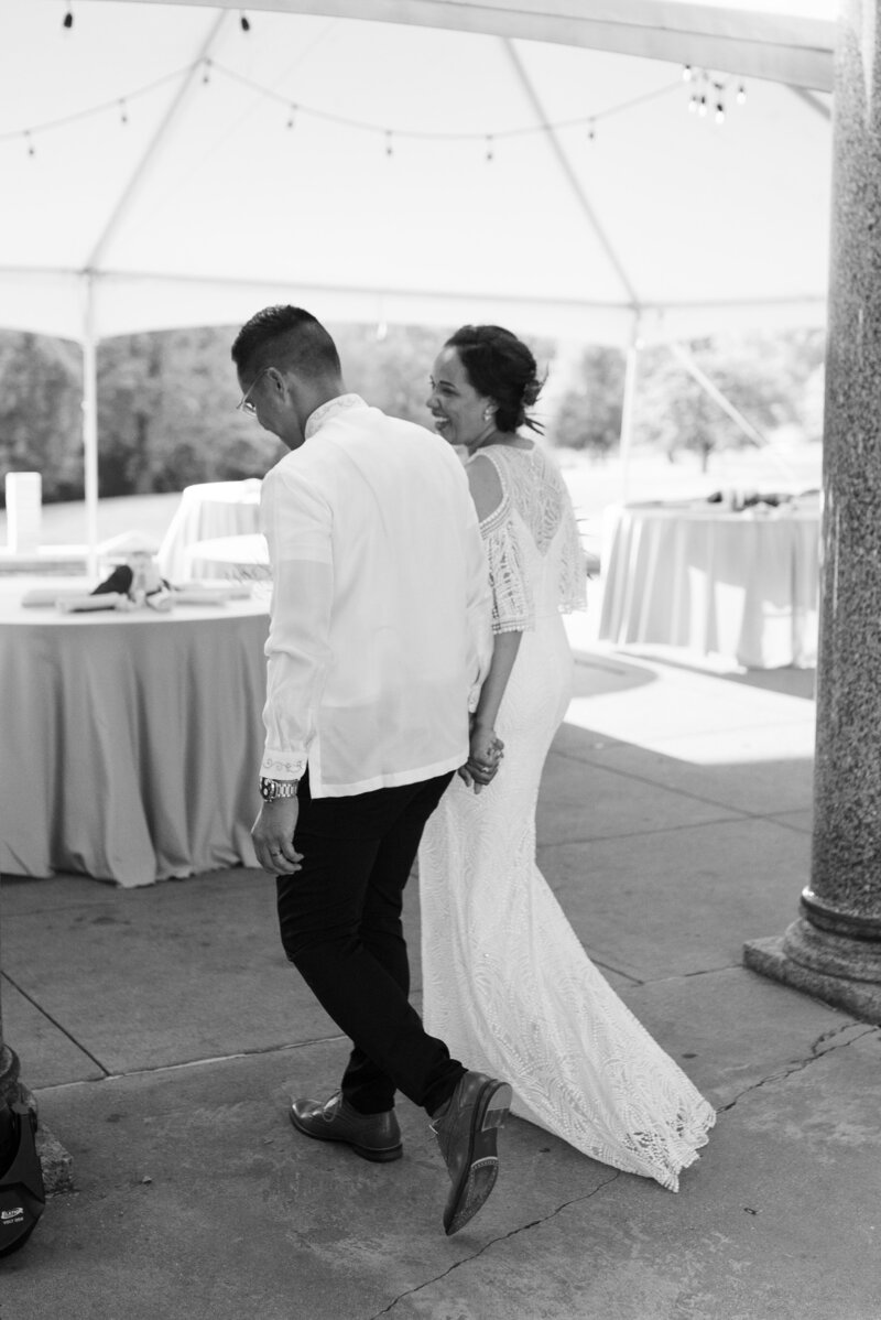 bride and groom walking away while holding hands black and white photo