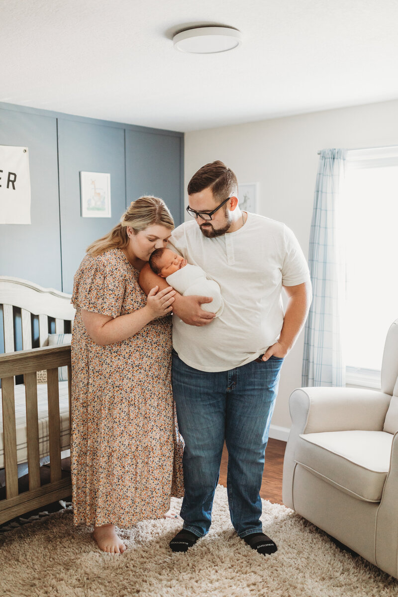 father holding baby while mother kisses top of baby's head