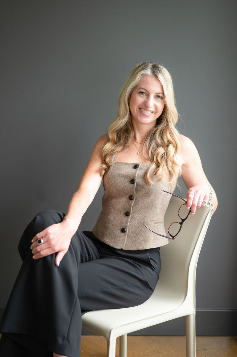 Liz Walton headshot sitting down on white chair with brown top and black pants