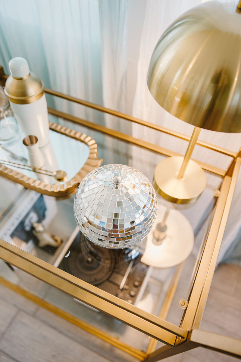 gold metal bar cart with disco ball canister, bar set, and gold lamp
