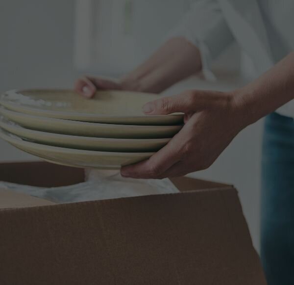 woman unpacking a moving box, taking out a stack of four plates