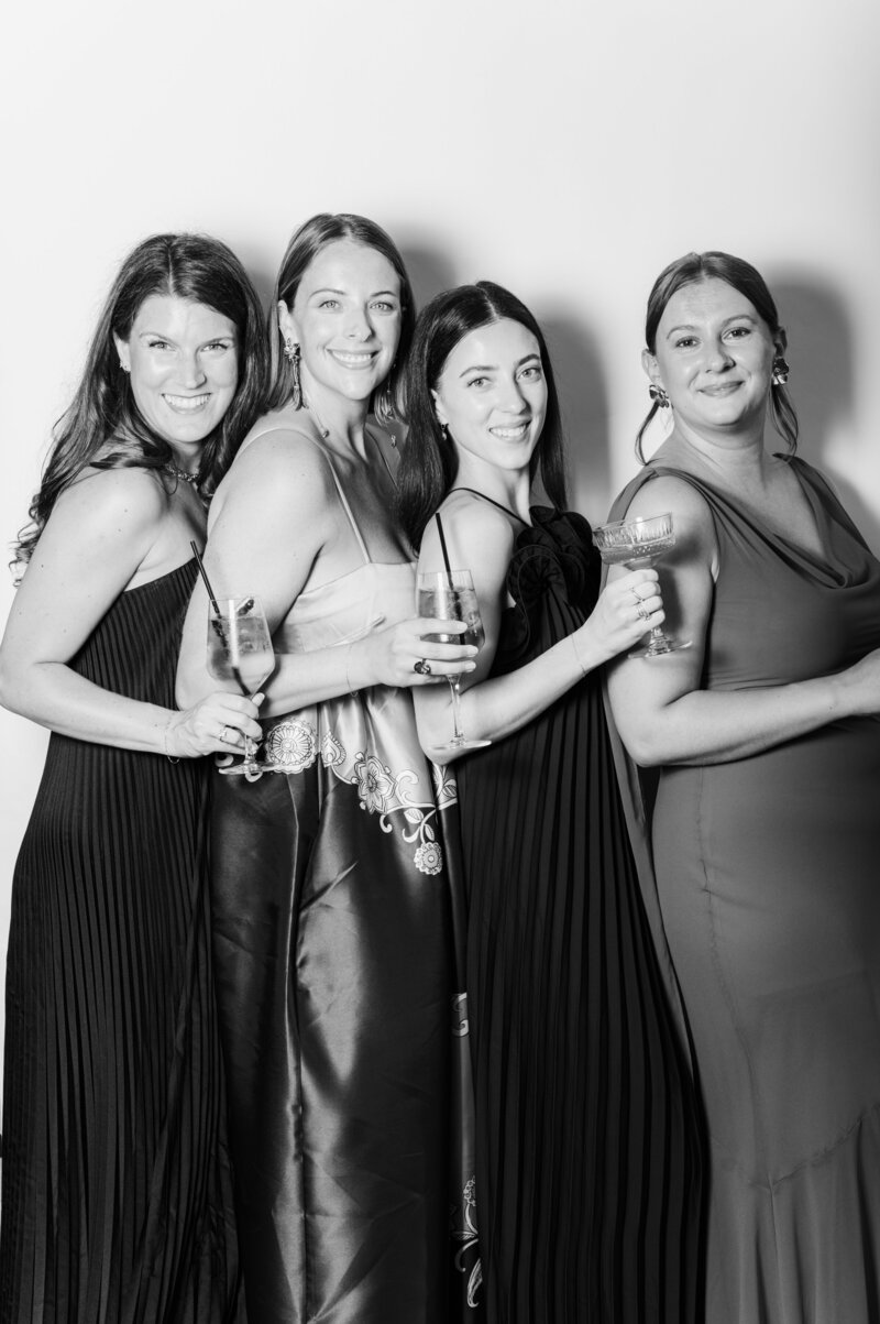 Elegant black and white group portrait of four women in formal attire holding cocktails at a Vogue Portrait photo booth in Richmond, VA.