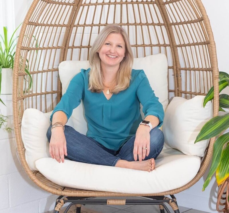 Maureen sitting crossed legged on chair smiling at camera