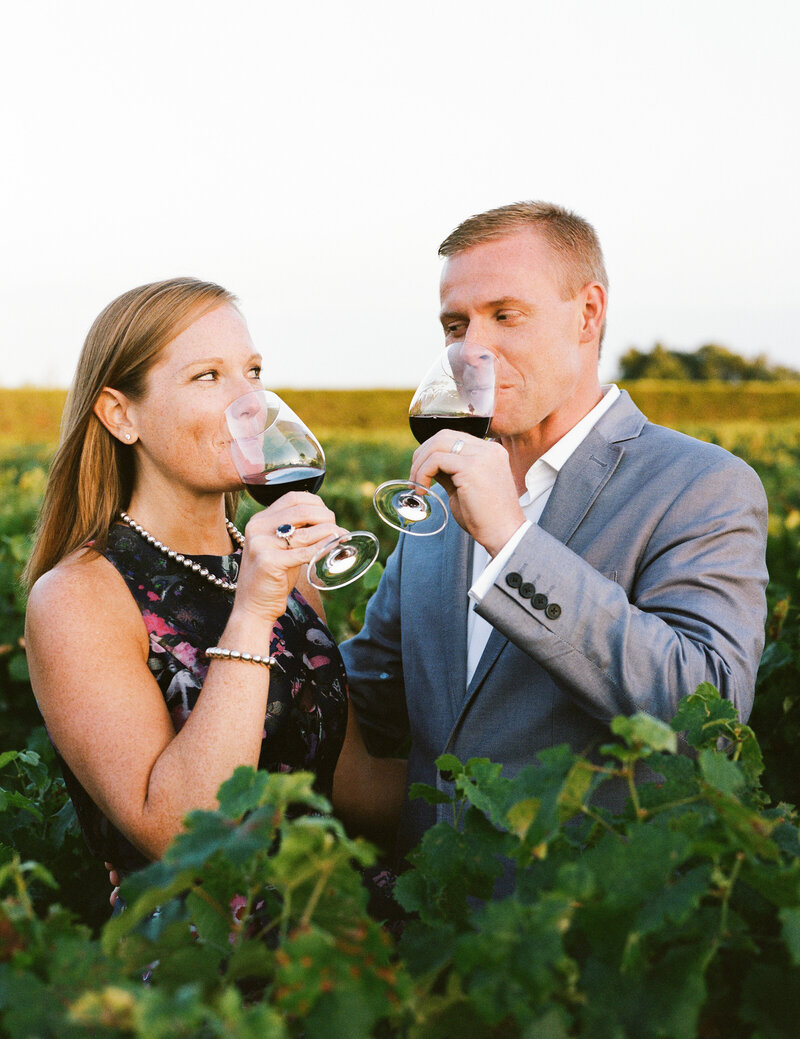 The couple in the vineyards, romantic pose drinking red wine at the sunset