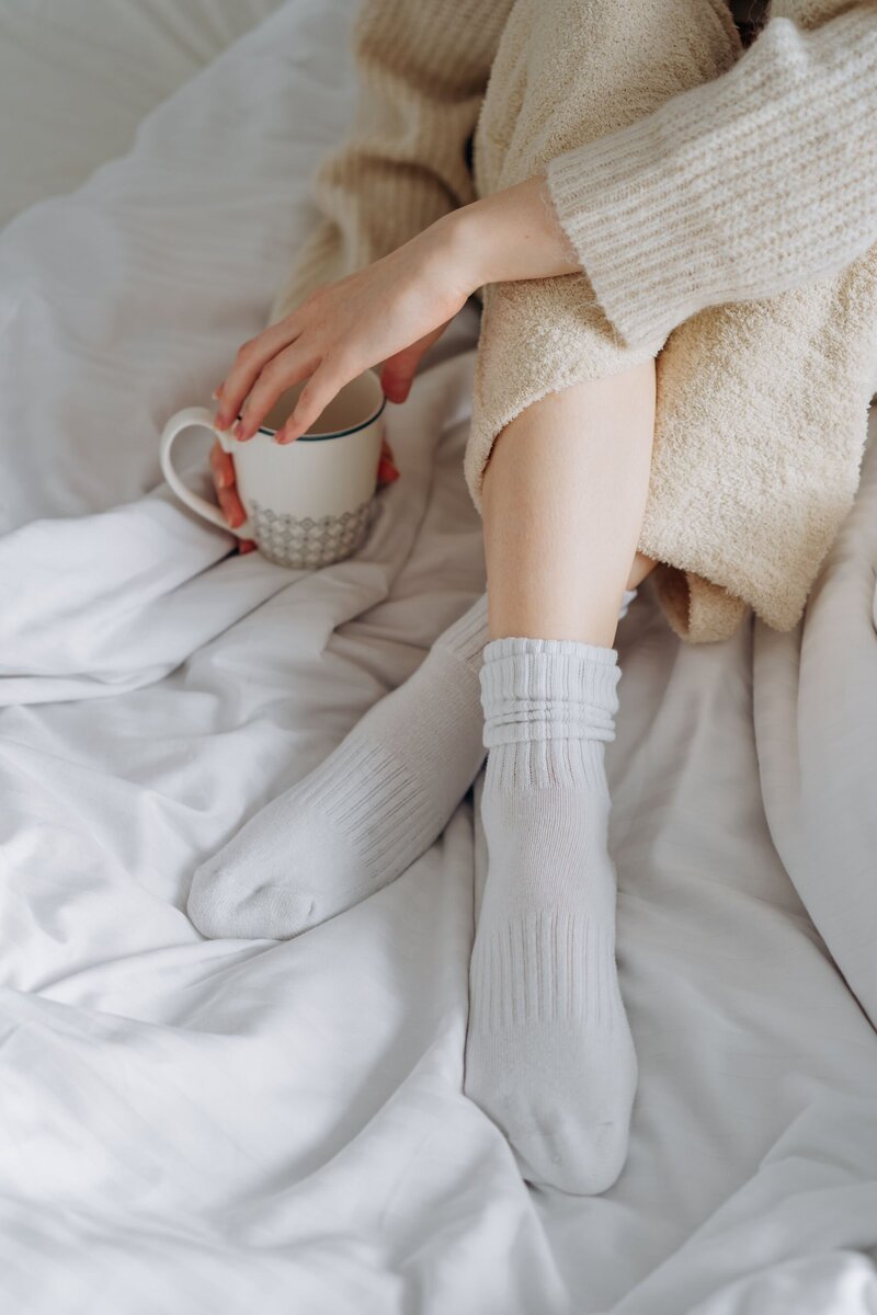 Person sits on bed with cup