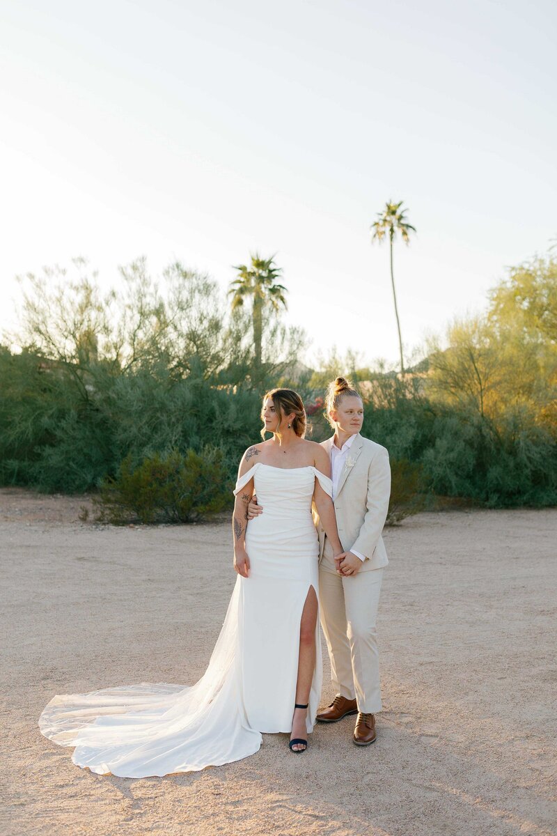 Two brides stand in the desert looking in opposite directions.