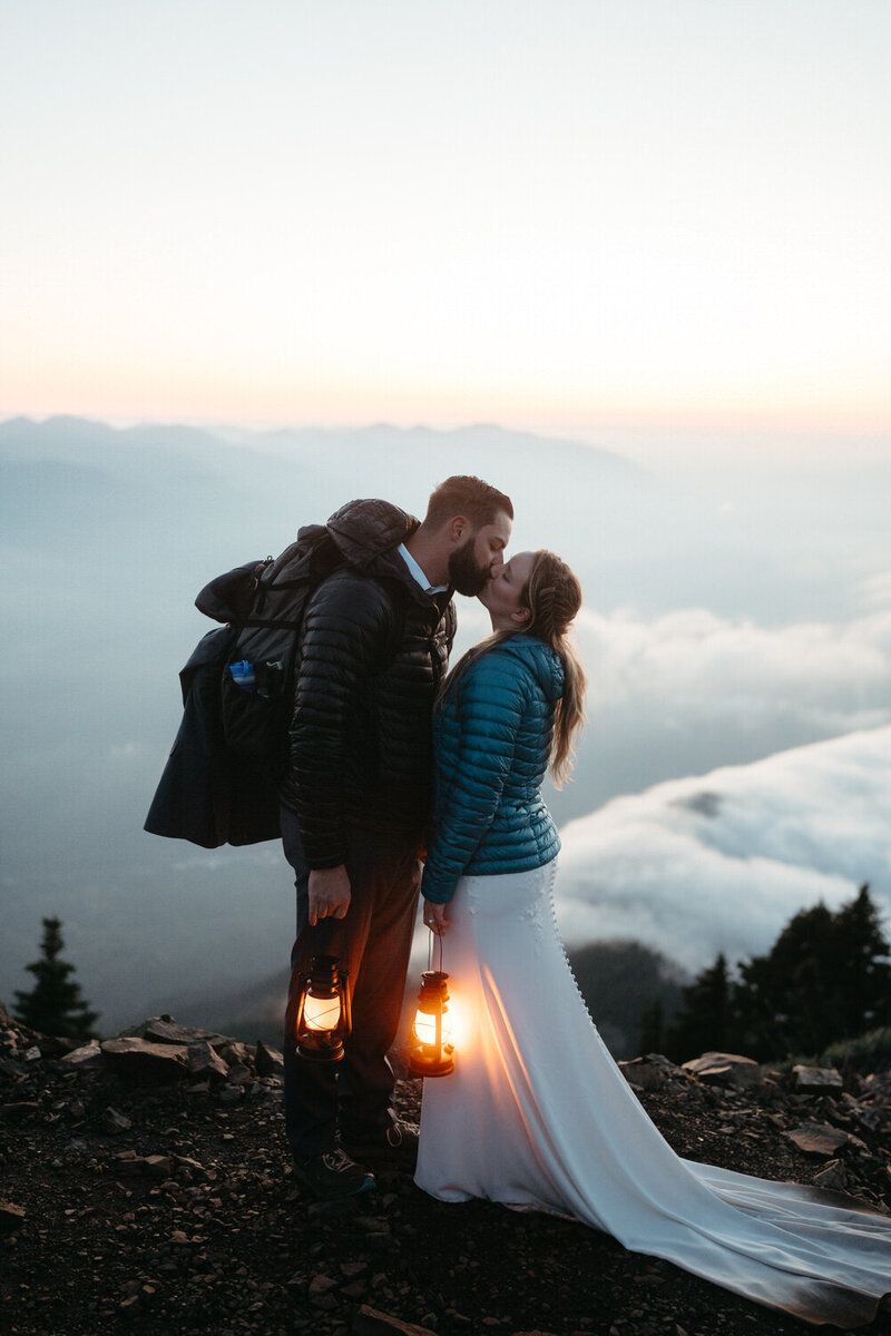 Adventurous couple holding lanterns and kissing on top of a mountain during their hiking elopement 