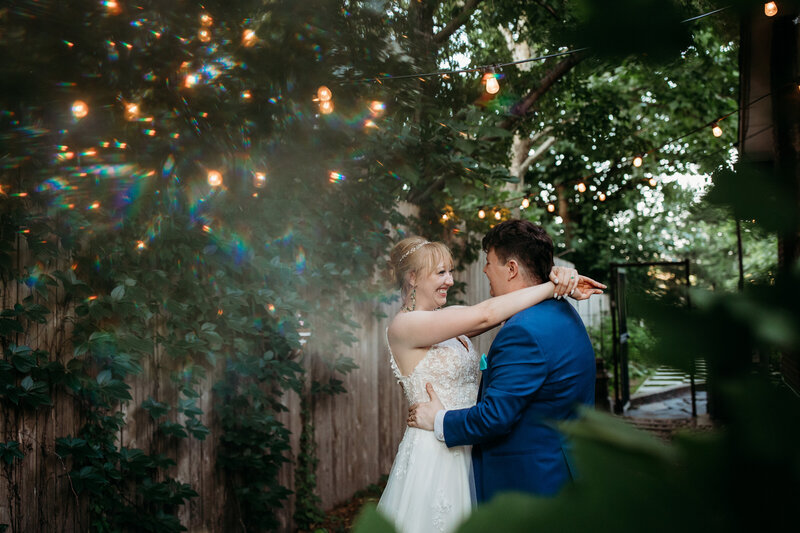 Bride and groom sharing a moment dancing under twinkling lights in a garden with lush greenery surrounding them