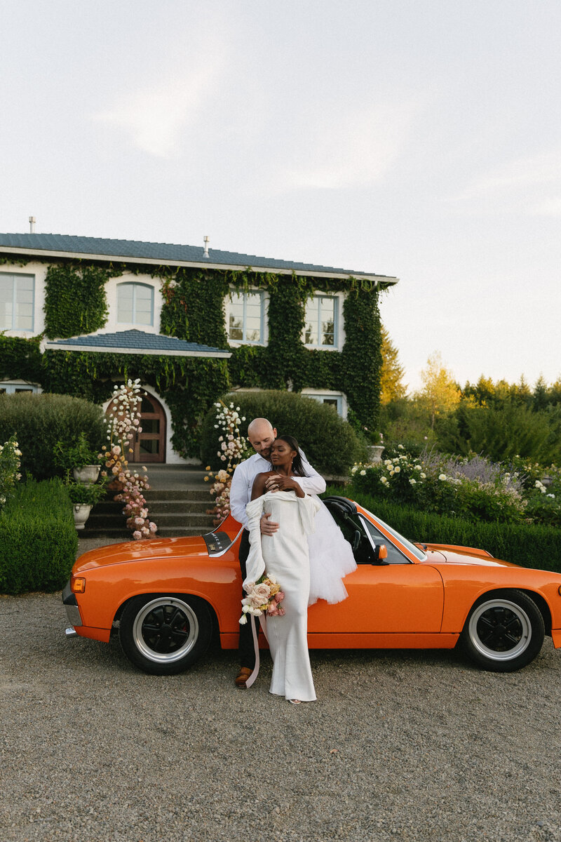 Wedding photos with bride and groom standing in front of an orange vintage car.