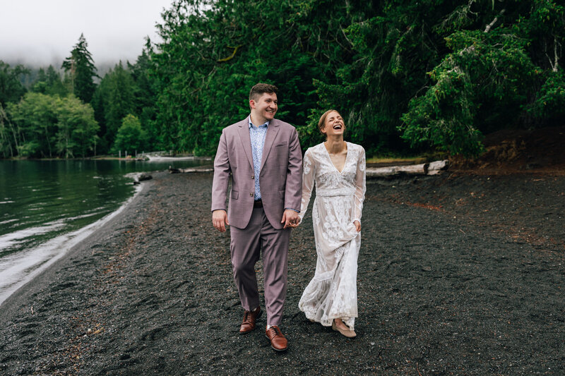 A bride and groom walk hand in hand along the shore of Lake Crescent for their Olympic National Park elopement in Washington.
