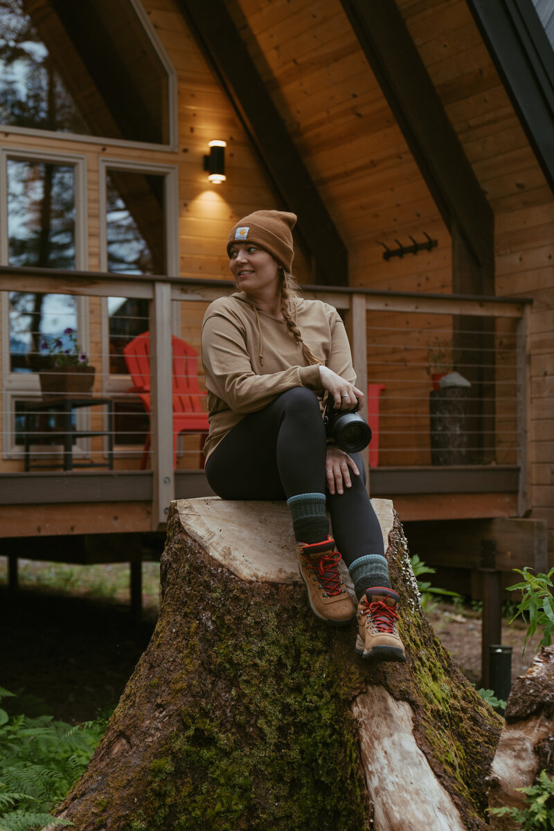 girl sitting on stump with camera in hand in Alaska