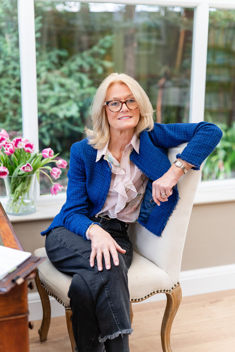 woman in blue blazer sitting on a chair looking into the camera