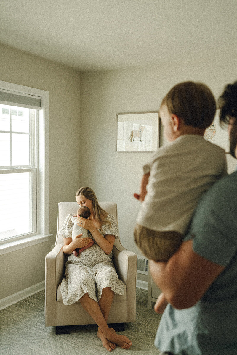 Mother holding her newborn baby while father looks on lovingly during a relaxed lifestyle newborn session in Northern Virginia