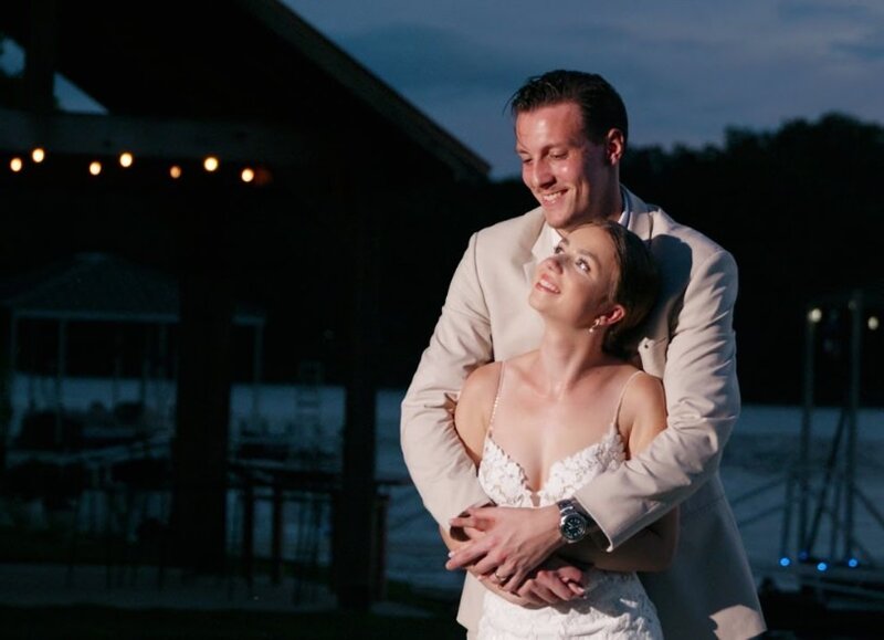 A person standing behind their partner with their arms around them on their wedding day 