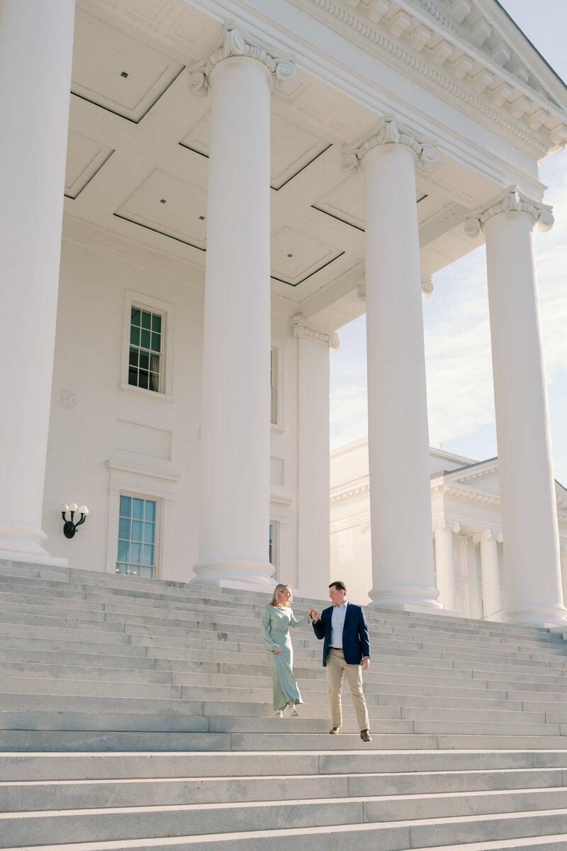 Virginia State Capitol Building Engagement Photos Richmond VA | newly engaged couple in green dress and blue suit walk hand in hand down the marble steps of the Capitol Building in Richmond, Virginia