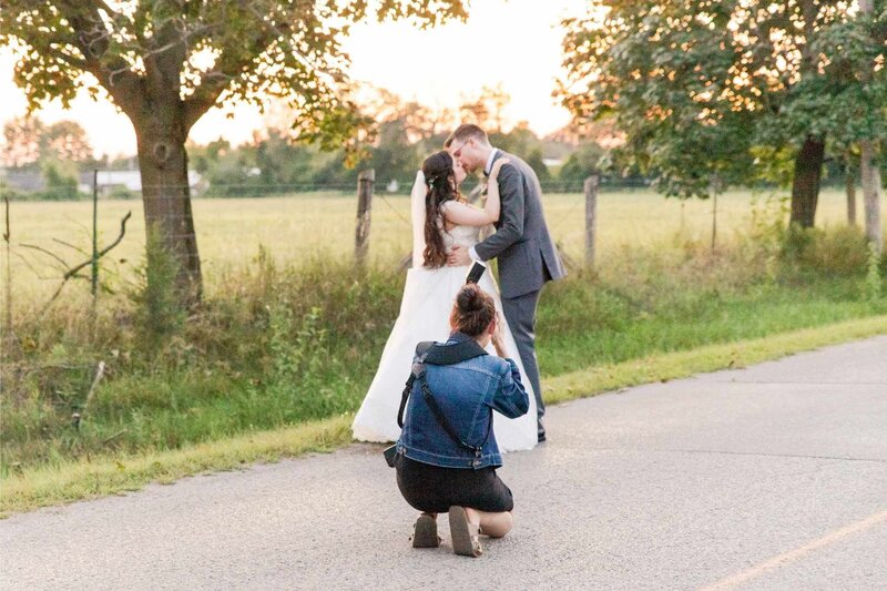 Wedding photographer kneeling on a country road capturing a bride and groom embracing at sunset, illustrating Simply Sandra Yvonne’s free wedding photography timeline template for planning smooth wedding days.