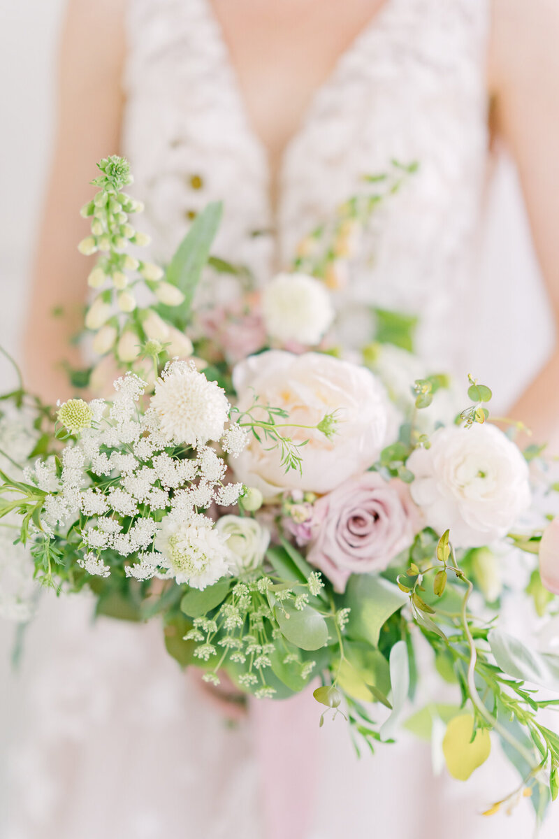 A bride holds a bouquet filled with garden roses, queen anne's lace, and honeysuckle vine.