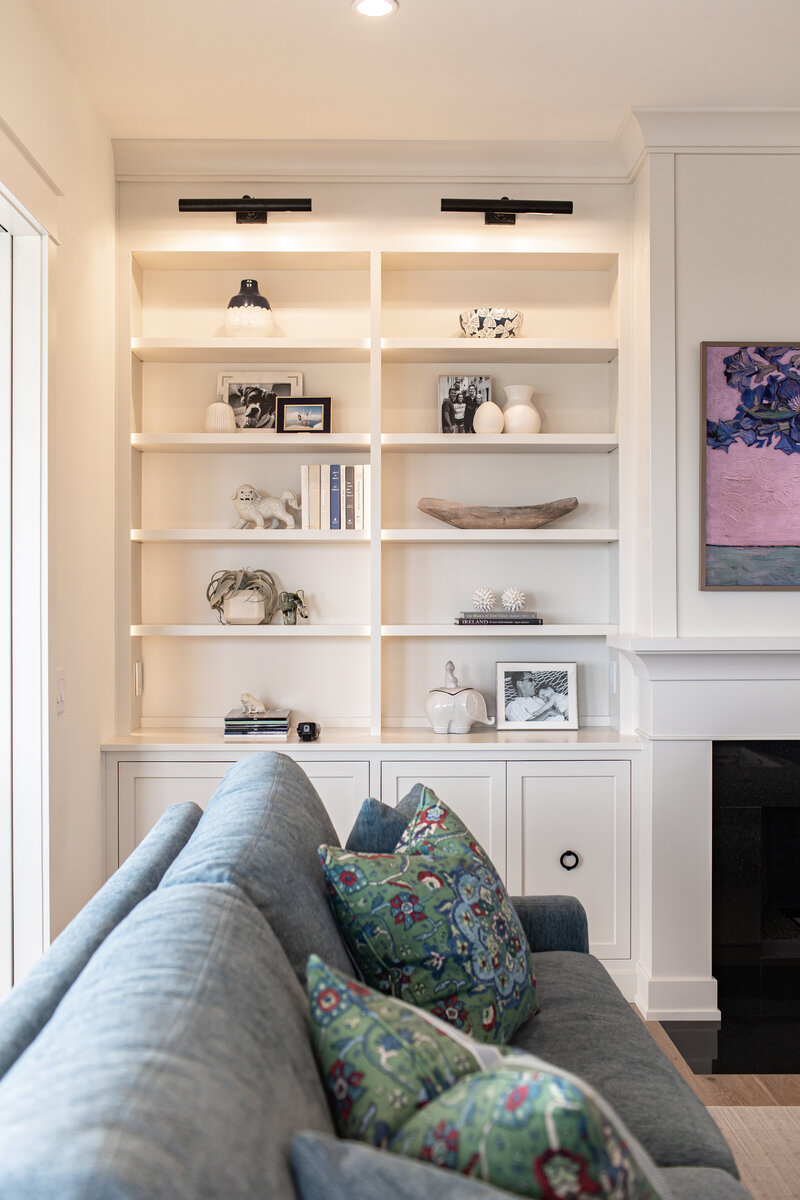 A cozy living area featuring custom built-ins next to a fireplace, with well-lit cabinets and a large couch adorned with decorative cushions. The design blends functionality with comfort, creating a warm and inviting space.