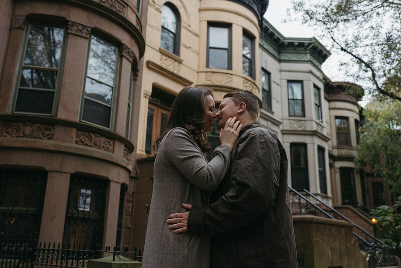 couple kissing in front of brownstones in NYC engagement photos, captured by Elsie Goodman, an NYC engagement and couples photographer