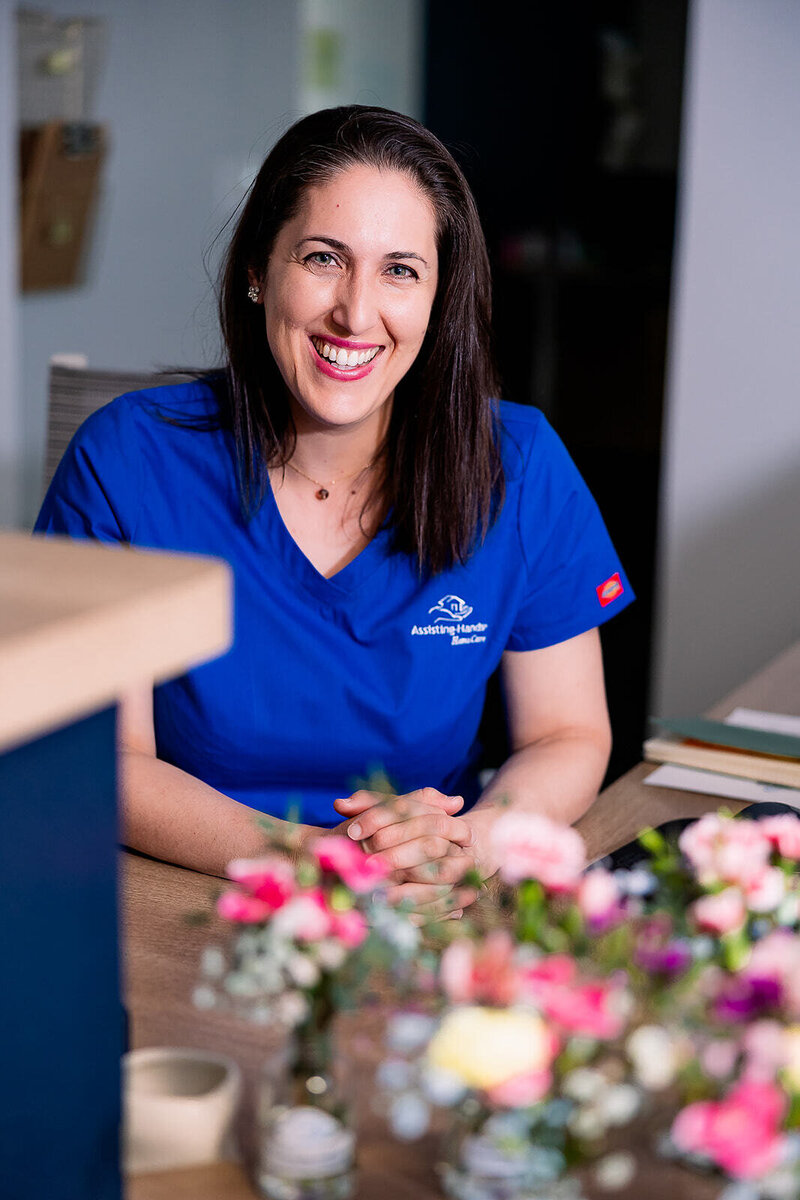 Woman smiling in blue scrubs behind a desk with flowers
