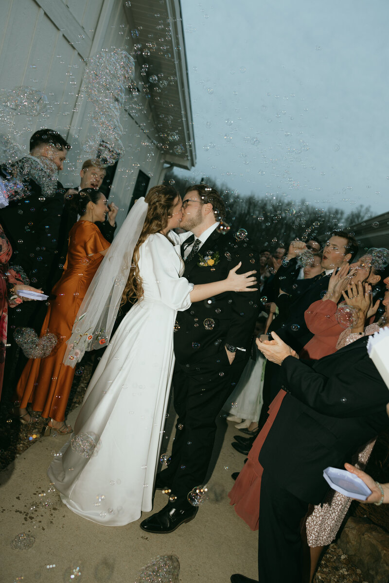 Bride and groom kiss as bubbles float around them