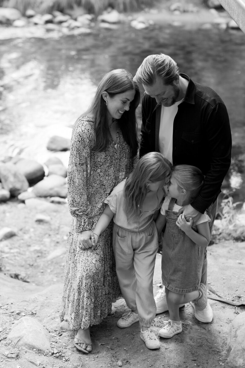 A black and white photo of a family standing by a riverside looking at eachother and smiling