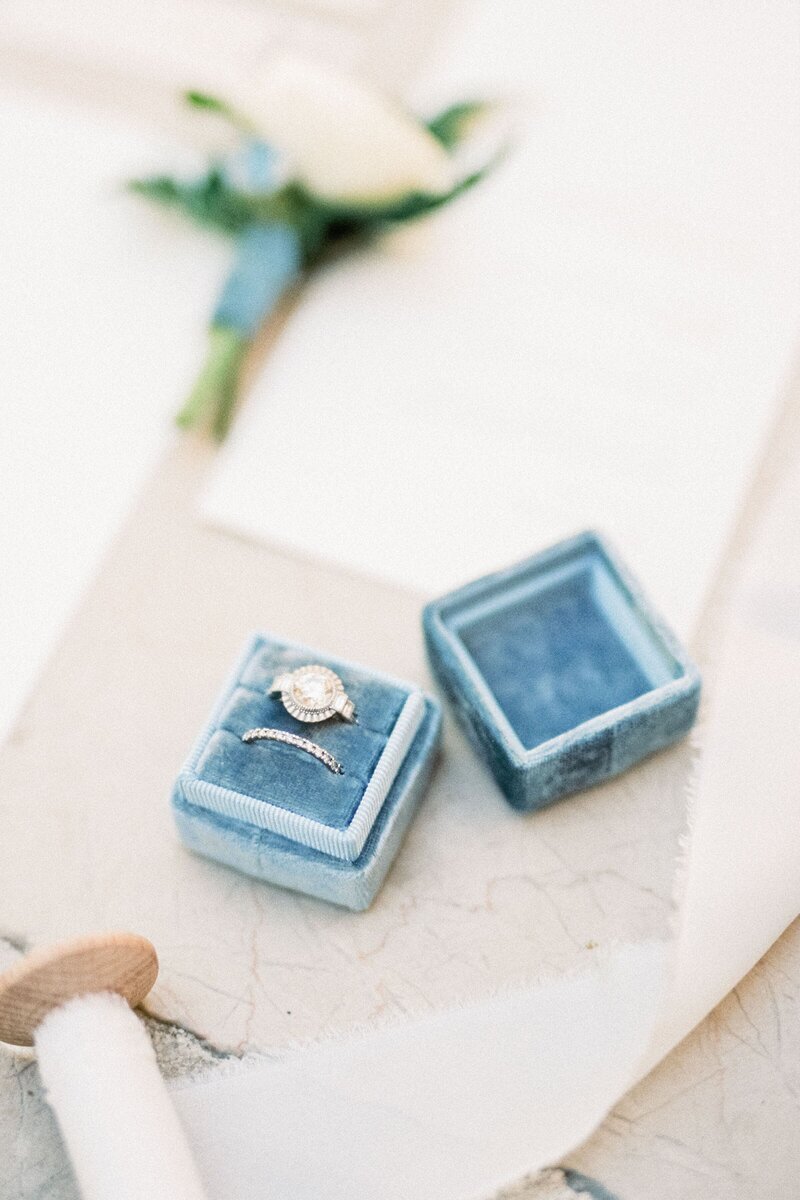 wedding-rings-lie-box-table-near-invitations-white-ribbon-reel