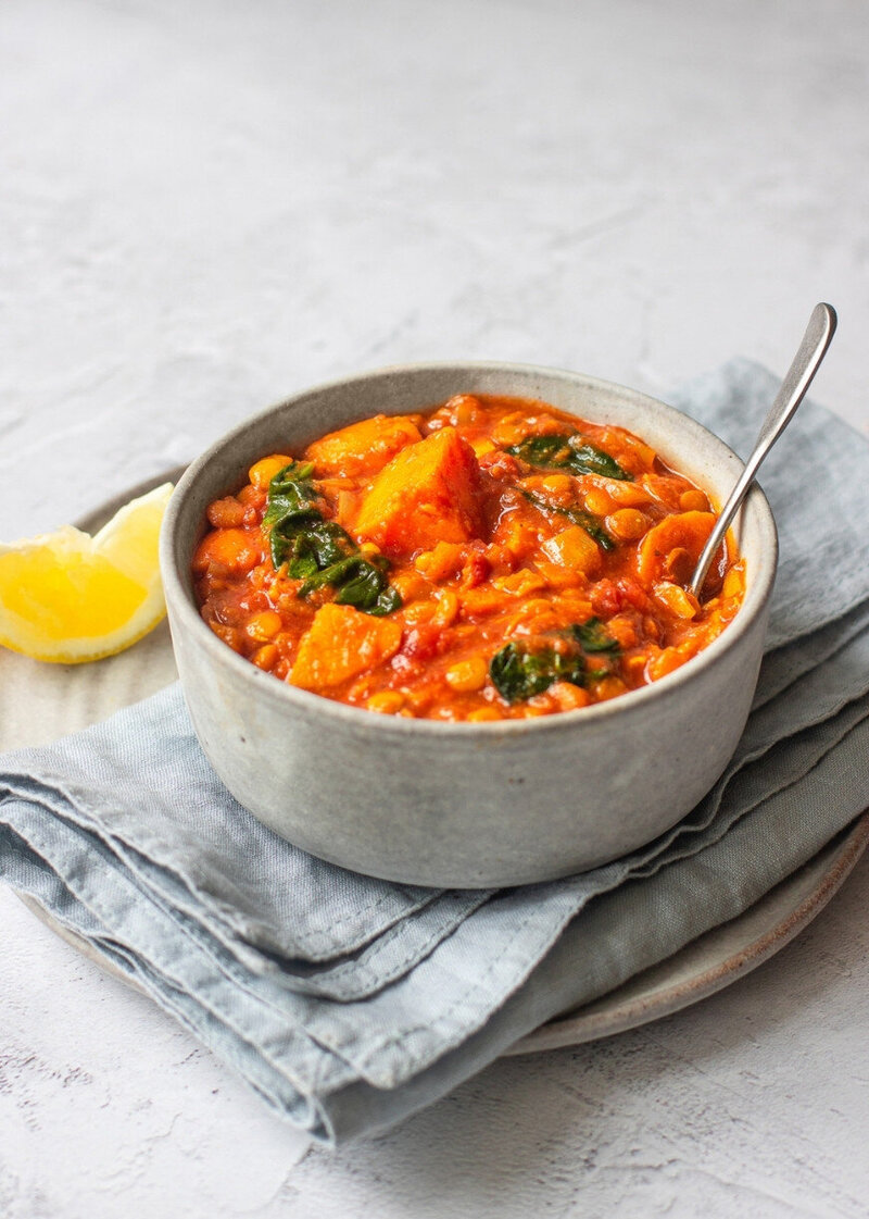 A vibrant menopause-friendly abundance bowl with lemony sweet potato and lentil curry, served with wilted greens and a wedge of lemon on a linen napkin. Part of the Menopause.Rescripted Recipe Vault.