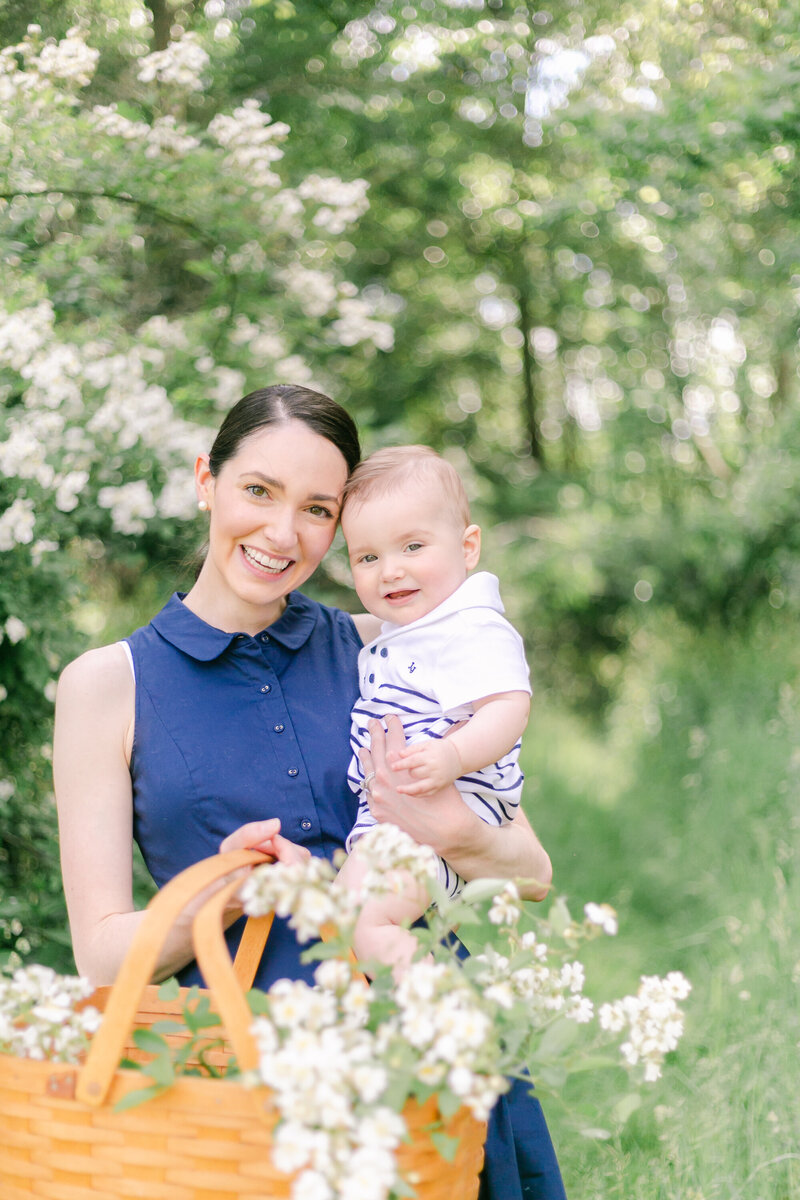 A mother holds her baby, both smiling, in a springtime portrait session by Rochester NY family photographer Emi Rose Studio.