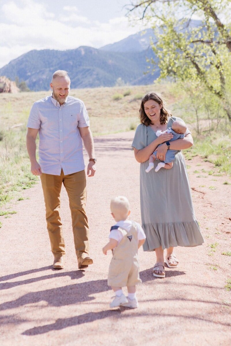 A mother and father walk down a dirt path holding a baby and looking at their toddler.