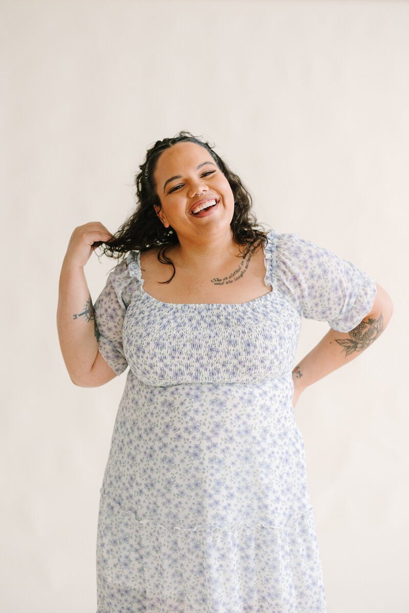 A person smiling with one hand on her hip and the other in her hair