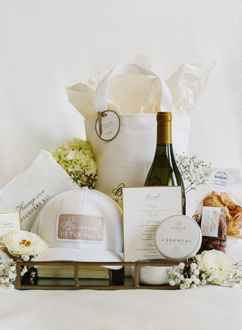 A “Brunch in the Hills” gift set with champagne, local bakery items, a baseball cap, a hangover recovery kit, and other items in a tray with flowers