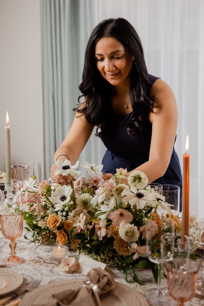 Portrait of Kathiya, owner of Zela Events styling a table with elegant floral arrangements.