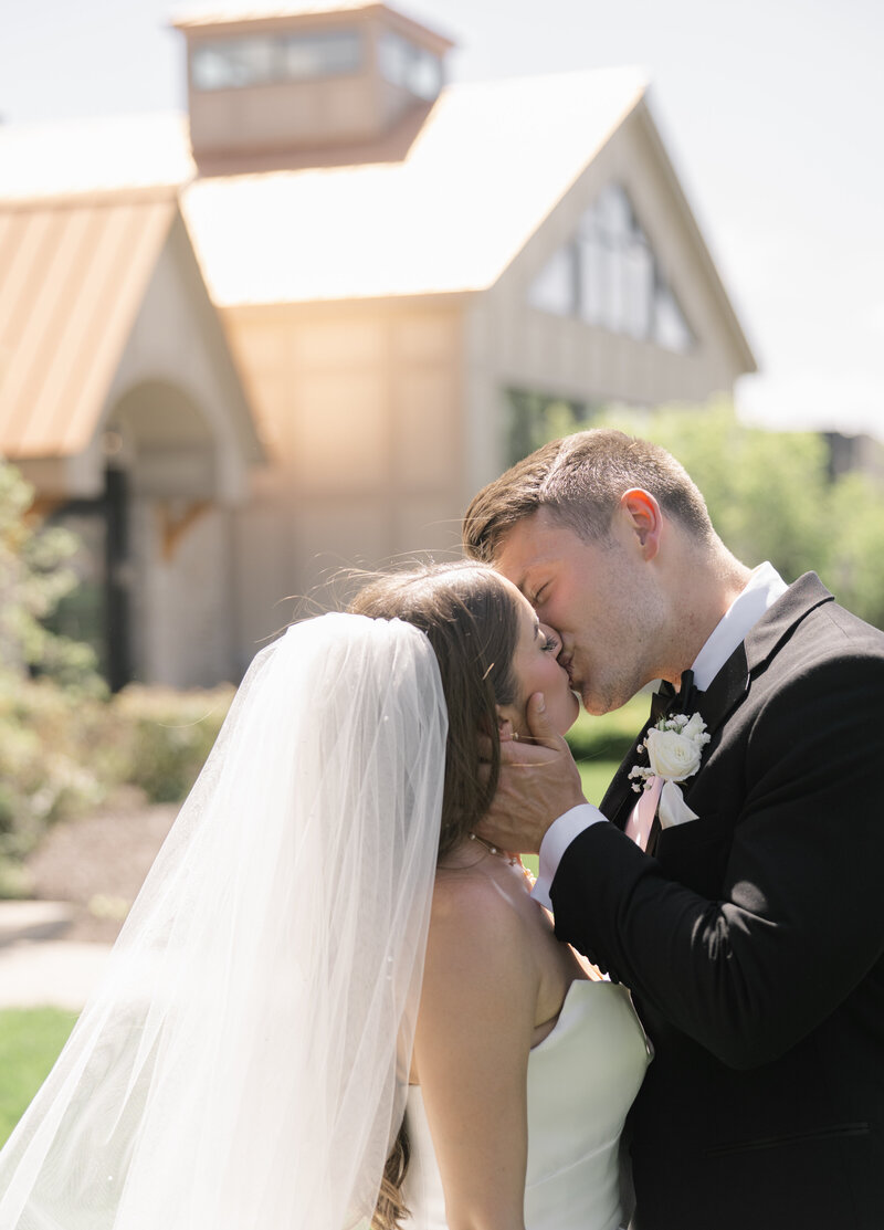 A closeup image of a bride and groom kiss in front of their wedding venue in the summertime at Venue3Two