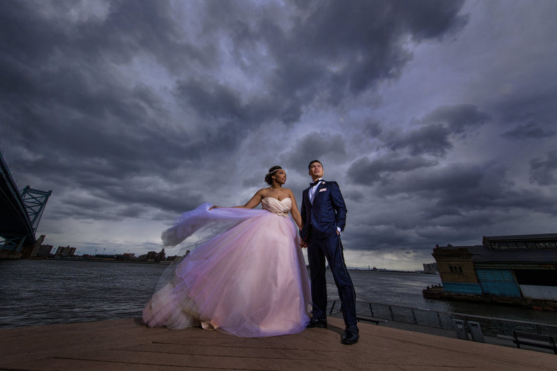 Bride and groom standing together under dramatic stormy skies at Race Street Pier in Philadelphia.